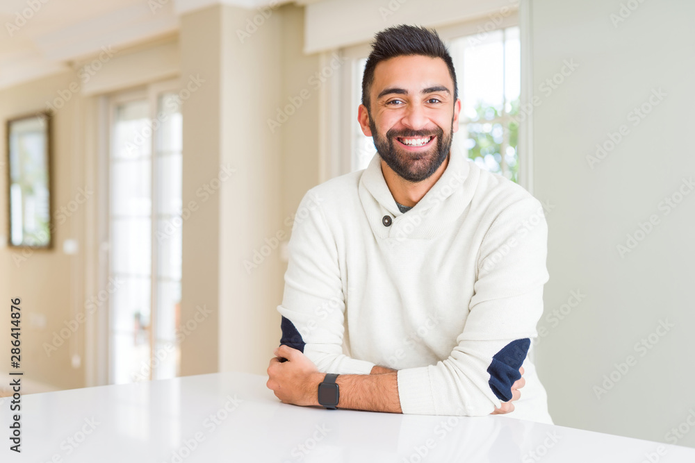 Handsome hispanic man wearing casual white sweater at home happy face smiling with crossed arms looking at the camera. Positive person.