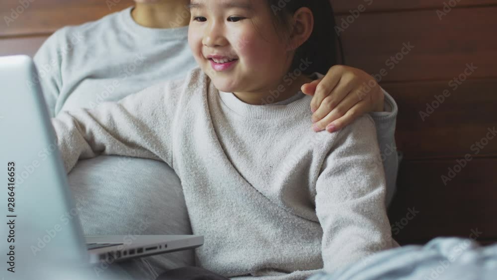 One happy little asian girl using laptop with her pregnant mother in ...