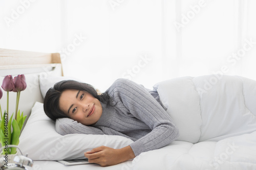 Woman lying on bed and using tablet in bedroom..