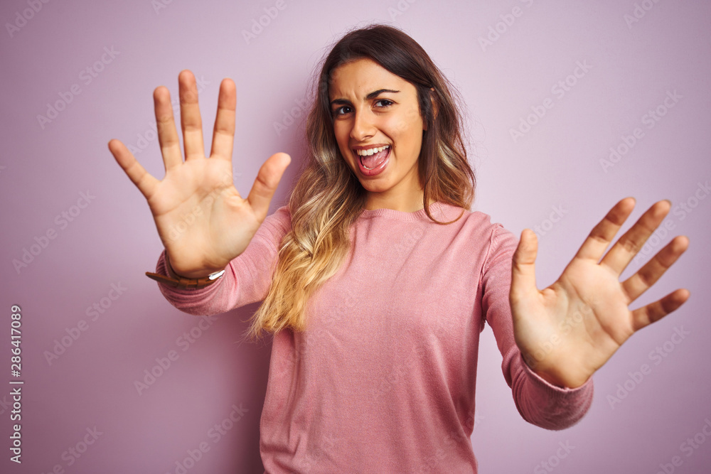 Young beautiful woman wearing a sweater over pink isolated background afraid and terrified with fear expression stop gesture with hands, shouting in shock. Panic concept. Young beautiful woman wearing a sweater over pink isolated background afraid and terrified with fear expression stop gesture with hands, shouting in shock. Panic concept.