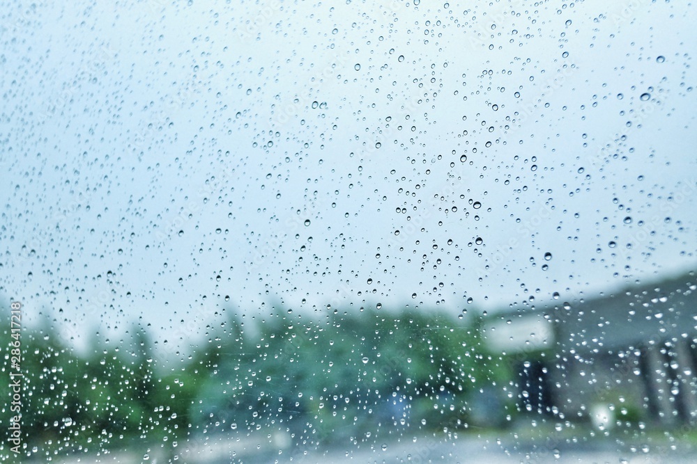Rain drops on car window with heavy rainy day with dramatic weather and blurred green nature background 