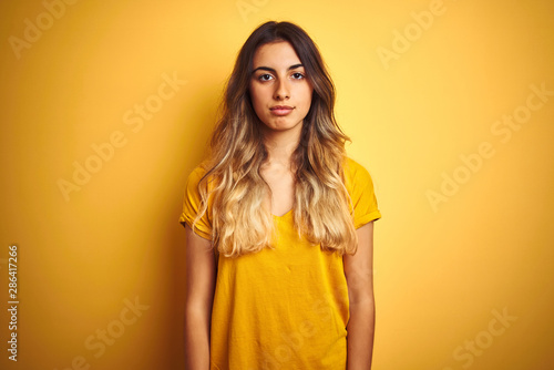 Young beautiful woman wearing t-shirt over yellow isolated background with serious expression on face. Simple and natural looking at the camera.