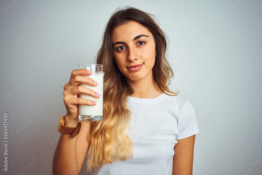Young beautiful woman drinking a glass of milk over white isolated background with a confident expression on smart face thinking serious Young beautiful woman drinking a glass of milk over white isolated background with a confident expression on smart face thinking serious