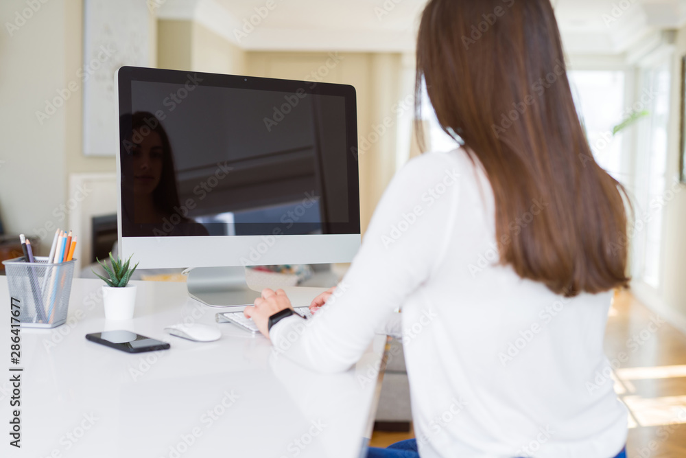 Young woman smiling working using computer and showing a blank screen on the background Young woman smiling working using computer and showing a blank screen on the background
