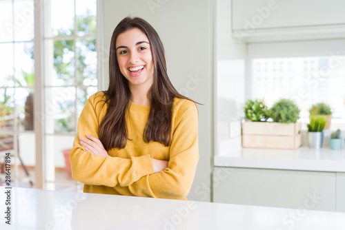 Beautiful young woman wearing yellow sweater happy face smiling with crossed arms looking at the camera. Positive person.