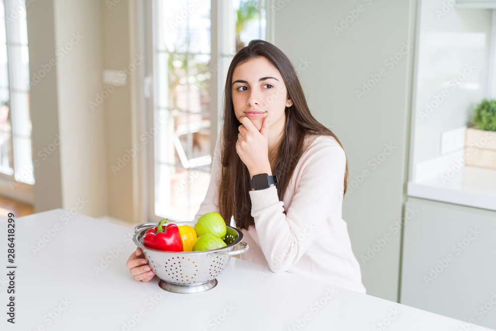 Beautiful young woman using colander to wash and clean vegatables serious face thinking about question, very confused idea Beautiful young woman using colander to wash and clean vegatables serious face thinking about question, very confused idea