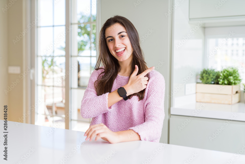 Beautiful young woman wearing pink sweater cheerful with a smile of face pointing with hand and finger up to the side with happy and natural expression on face Beautiful young woman wearing pink sweater cheerful with a smile of face pointing with hand and finger up to the side with happy and natural expression on face