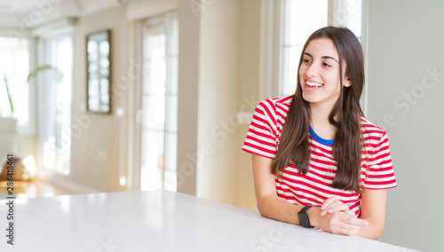 Beautiful young woman wearing casual stripes t-shirt looking away to side with smile on face, natural expression. Laughing confident.
