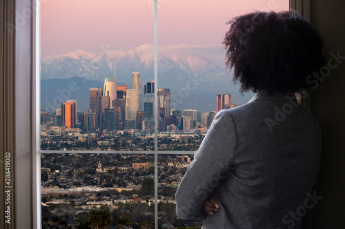 Black female business woman looking out the window of an office in Los Angeles.  She looks like a female architect thinking of urban development or a city mayor or governor planning zoning laws.