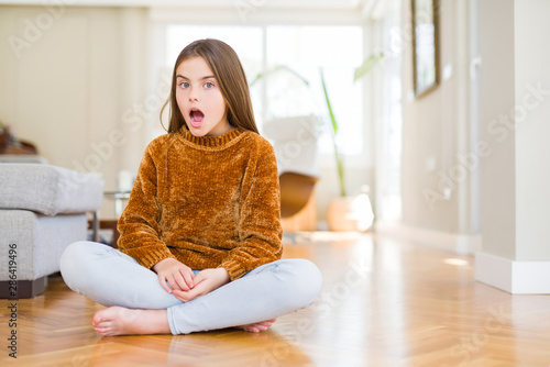 Beautiful young girl kid sitting on the floor at home afraid and shocked with surprise expression, fear and excited face.