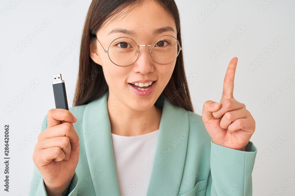 Young chinese businesswoman holding usb memory over isolated white background surprised with an idea or question pointing finger with happy face, number one Young chinese businesswoman holding usb memory over isolated white background surprised with an idea or question pointing finger with happy face, number one
