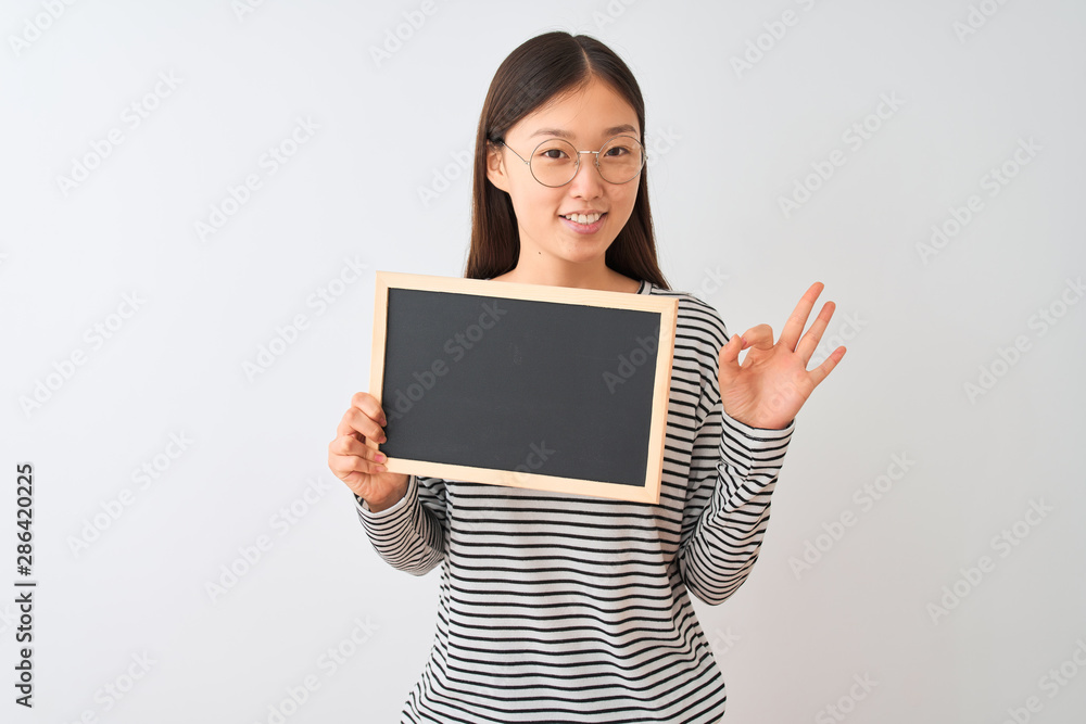 Young chinese woman wearing glasses holding blackboard over isolated white background doing ok sign with fingers, excellent symbol Young chinese woman wearing glasses holding blackboard over isolated white background doing ok sign with fingers, excellent symbol