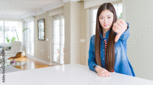 Young beautiful asian woman with long hair wearing denim jacket looking unhappy and angry showing rejection and negative with thumbs down gesture. Bad expression.