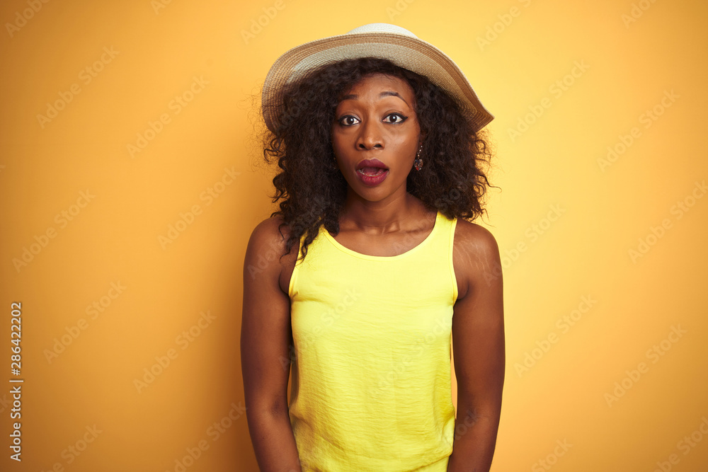 Young african american woman wearing t-shirt and hat over isolated yellow background afraid and shocked with surprise expression, fear and excited face. Young african american woman wearing t-shirt and hat over isolated yellow background afraid and shocked with surprise expression, fear and excited face.