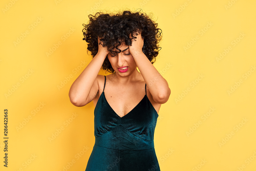 Young arab woman with curly hair wearing elegant dress over isolated yellow background suffering from headache desperate and stressed because pain and migraine. Hands on head. Young arab woman with curly hair wearing elegant dress over isolated yellow background suffering from headache desperate and stressed because pain and migraine. Hands on head.