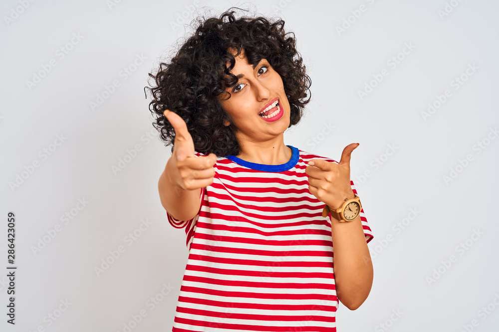Young arab woman with curly hair wearing striped t-shirt over isolated white background pointing fingers to camera with happy and funny face. Good energy and vibes. Young arab woman with curly hair wearing striped t-shirt over isolated white background pointing fingers to camera with happy and funny face. Good energy and vibes.