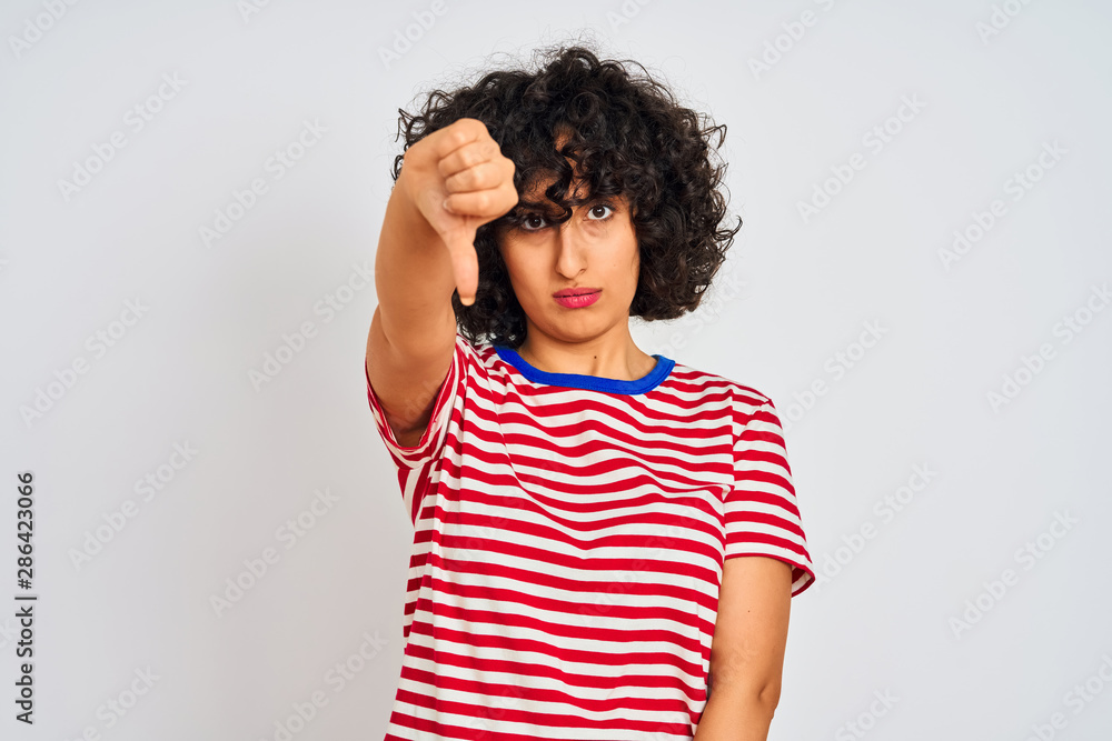Young arab woman with curly hair wearing striped t-shirt over isolated white background looking unhappy and angry showing rejection and negative with thumbs down gesture. Bad expression. Young arab woman with curly hair wearing striped t-shirt over isolated white background looking unhappy and angry showing rejection and negative with thumbs down gesture. Bad expression.