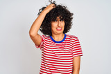 Young arab woman with curly hair wearing striped t-shirt over isolated white background confuse and wonder about question. Uncertain with doubt, thinking with hand on head. Pensive concept.