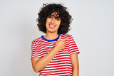 Young arab woman with curly hair wearing striped t-shirt over isolated white background cheerful with a smile of face pointing with hand and finger up to the side with happy and natural expression