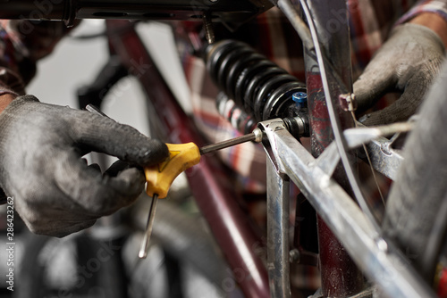 Cropped shot of man mechanic working in bicycle repair shop, worker repairing mountain bike using special tool, wearing protective gloves