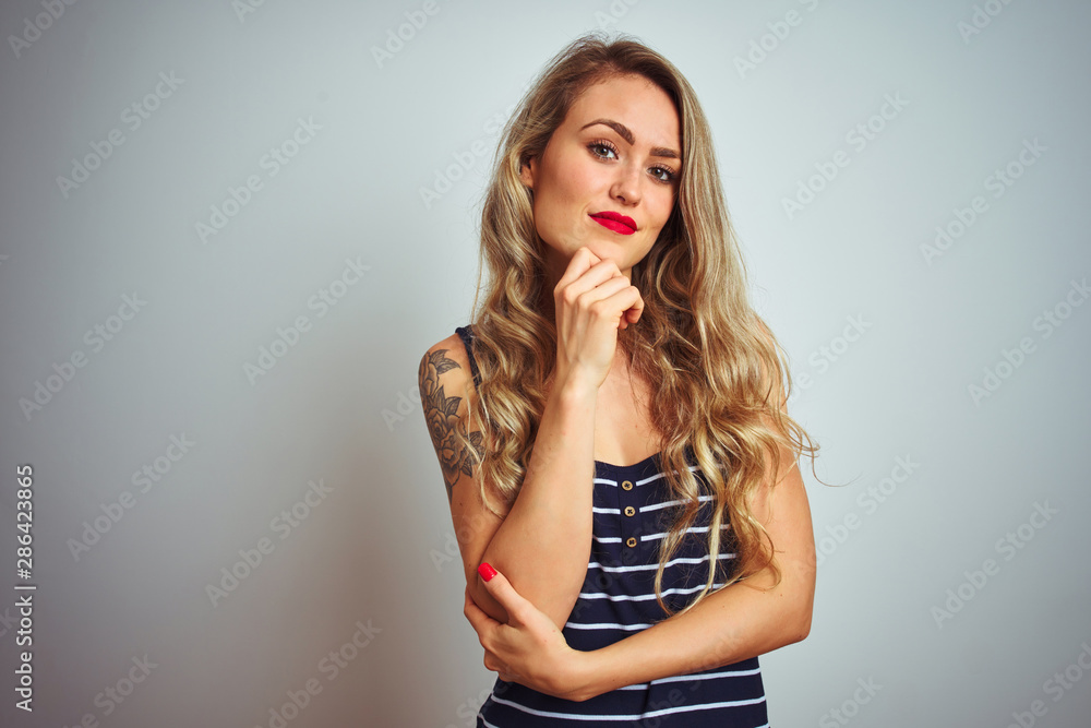 Young beautiful woman wearing stripes t-shirt standing over white isolated background looking confident at the camera smiling with crossed arms and hand raised on chin. Thinking positive. Young beautiful woman wearing stripes t-shirt standing over white isolated background looking confident at the camera smiling with crossed arms and hand raised on chin. Thinking positive.