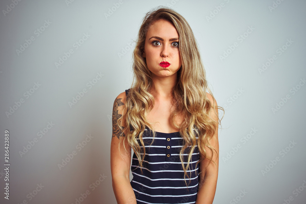 Young beautiful woman wearing stripes t-shirt standing over white isolated background puffing cheeks with funny face. Mouth inflated with air, crazy expression. Young beautiful woman wearing stripes t-shirt standing over white isolated background puffing cheeks with funny face. Mouth inflated with air, crazy expression.