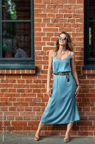 girl in blue dress and sunglasses posing on background of brick wall