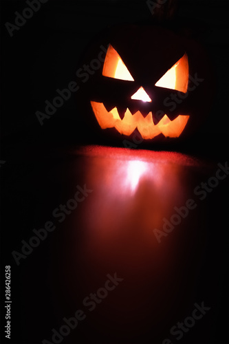 Halloween October holiday celebration symbol, scary pumpkin glowing with reflection, black background