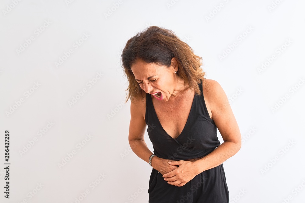 Middle age woman wearing black casual dress standing over isolated white background with hand on stomach because nausea, painful disease feeling unwell. Ache concept. Middle age woman wearing black casual dress standing over isolated white background with hand on stomach because nausea, painful disease feeling unwell. Ache concept.