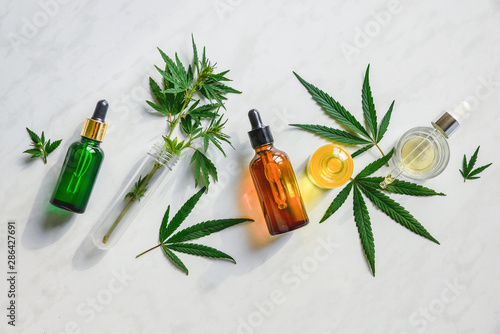 Various glass bottles with CBD oil, THC tincture and hemp leaves on a marble background. Flat lay, minimalism. Cosmetics CBD oil. photo
