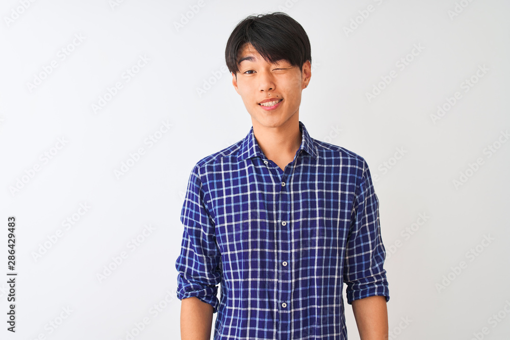 Young chinese man wearing casual blue shirt standing over isolated white background winking looking at the camera with sexy expression, cheerful and happy face. Young chinese man wearing casual blue shirt standing over isolated white background winking looking at the camera with sexy expression, cheerful and happy face.
