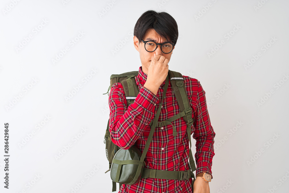 Chinese hiker man wearing backpack canteen glasses over isolated white background smelling something stinky and disgusting, intolerable smell, holding breath with fingers on nose. Bad smells concept. Chinese hiker man wearing backpack canteen glasses over isolated white background smelling something stinky and disgusting, intolerable smell, holding breath with fingers on nose. Bad smells concept.