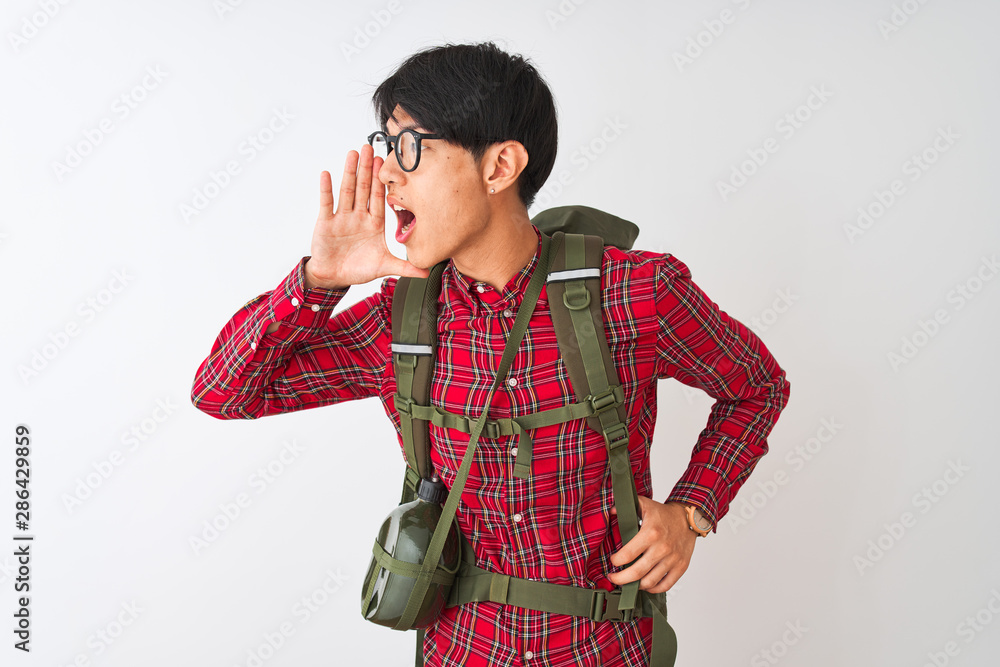 Chinese hiker man wearing backpack canteen glasses over isolated white background shouting and screaming loud to side with hand on mouth. Communication concept. Chinese hiker man wearing backpack canteen glasses over isolated white background shouting and screaming loud to side with hand on mouth. Communication concept.