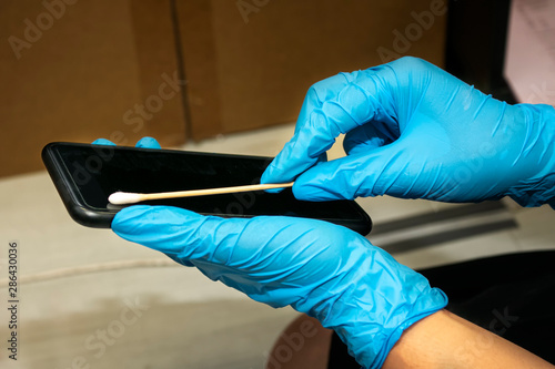 Hand holding cotton swab stick and swab dipped in diluted rubbing alcohol on screen of smartphone. Cleaning dirty screen phone for disease prevention from bacteria. Swap test device in laboratory.