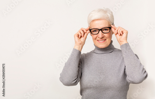Foto Beautiful elderly woman trying new glasses and looking to camera