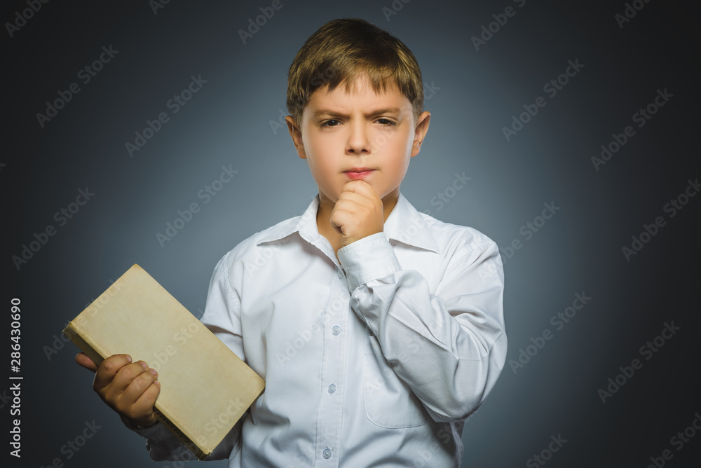 Closeup Thoughtful boy with with book isolated on gray background Closeup Thoughtful boy with with book isolated on gray background