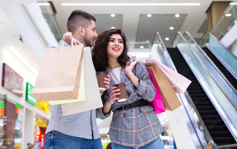Happy millennial couple resting in shopping mall, drinking coffee Happy millennial couple resting in shopping mall, drinking coffee