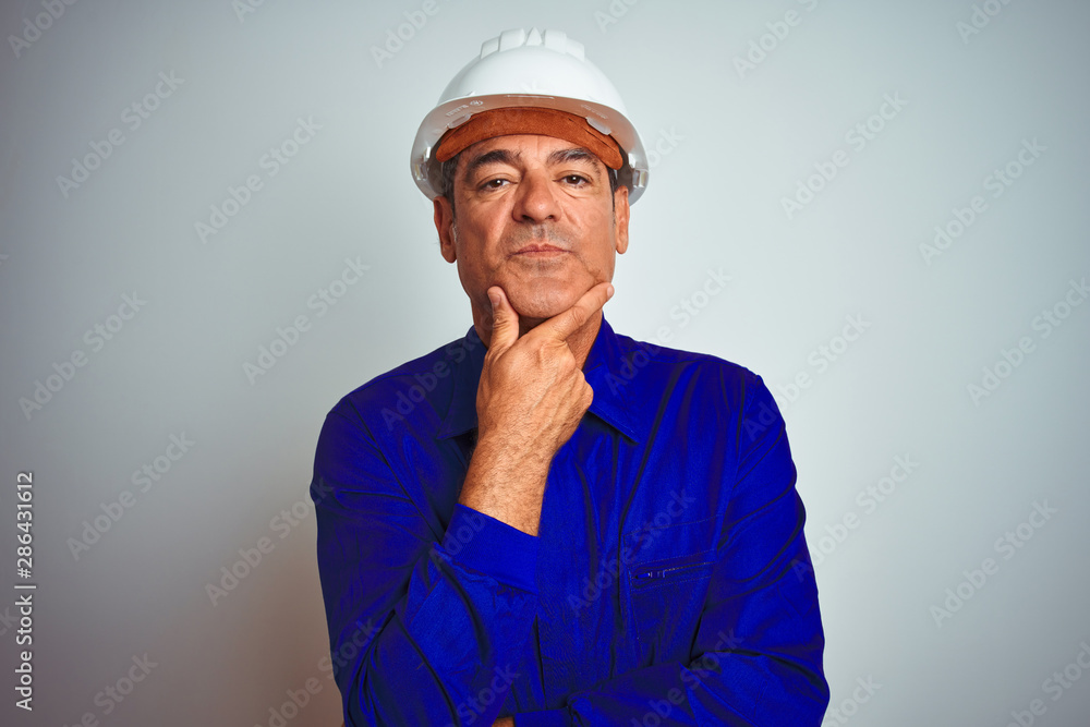 Handsome middle age worker man wearing uniform and helmet over isolated white background looking confident at the camera with smile with crossed arms and hand raised on chin. Thinking positive.