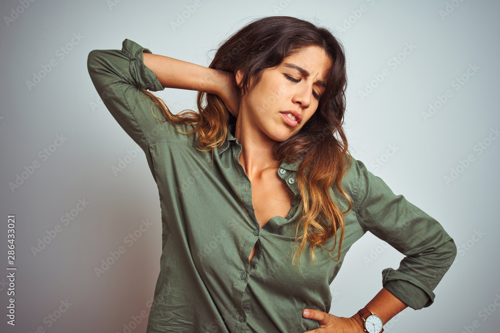 Young beautiful woman wearing green shirt standing over grey isolated background Suffering of neck ache injury, touching neck with hand, muscular pain Young beautiful woman wearing green shirt standing over grey isolated background Suffering of neck ache injury, touching neck with hand, muscular pain