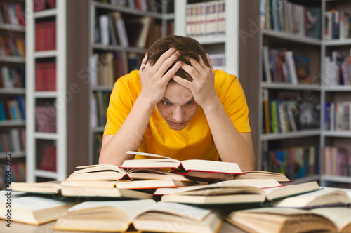 Exhausted guy holding his head and reading book in library photo