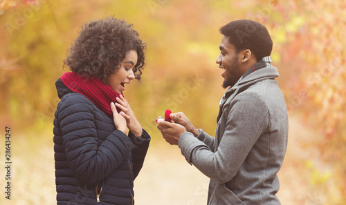 Romantic afro man proposing to woman in autumn park