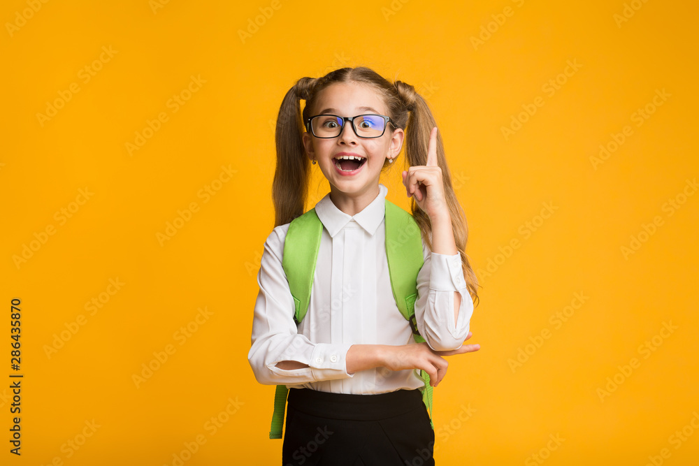 Funny Little Girl Pointing Finger Up On Yellow Studio Background