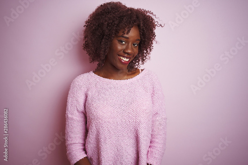 Young african afro woman wearing sweater standing over isolated pink background looking away to side with smile on face, natural expression. Laughing confident.