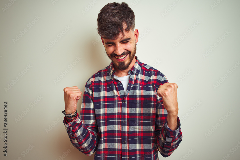 Fototapeta premium Young man wearing casual shirt standing over isolated white background very happy and excited doing winner gesture with arms raised, smiling and screaming for success. Celebration concept.