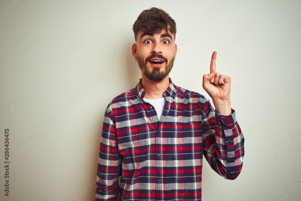 Young man wearing casual shirt standing over isolated white background pointing finger up with successful idea. Exited and happy. Number one. Young man wearing casual shirt standing over isolated white background pointing finger up with successful idea. Exited and happy. Number one.