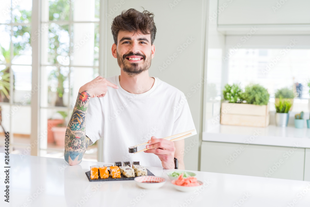 Young man eating asian sushi from home delivery with surprise face pointing finger to himself