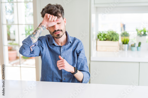 Young man wearing casual shirt sitting on white table Touching forehead for illness and fever, flu and cold, virus sick