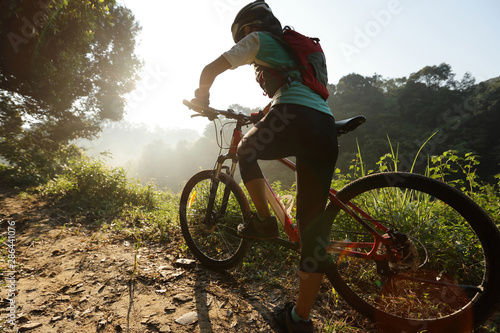 Young woman cyclist riding mountain bike on summer forest trail