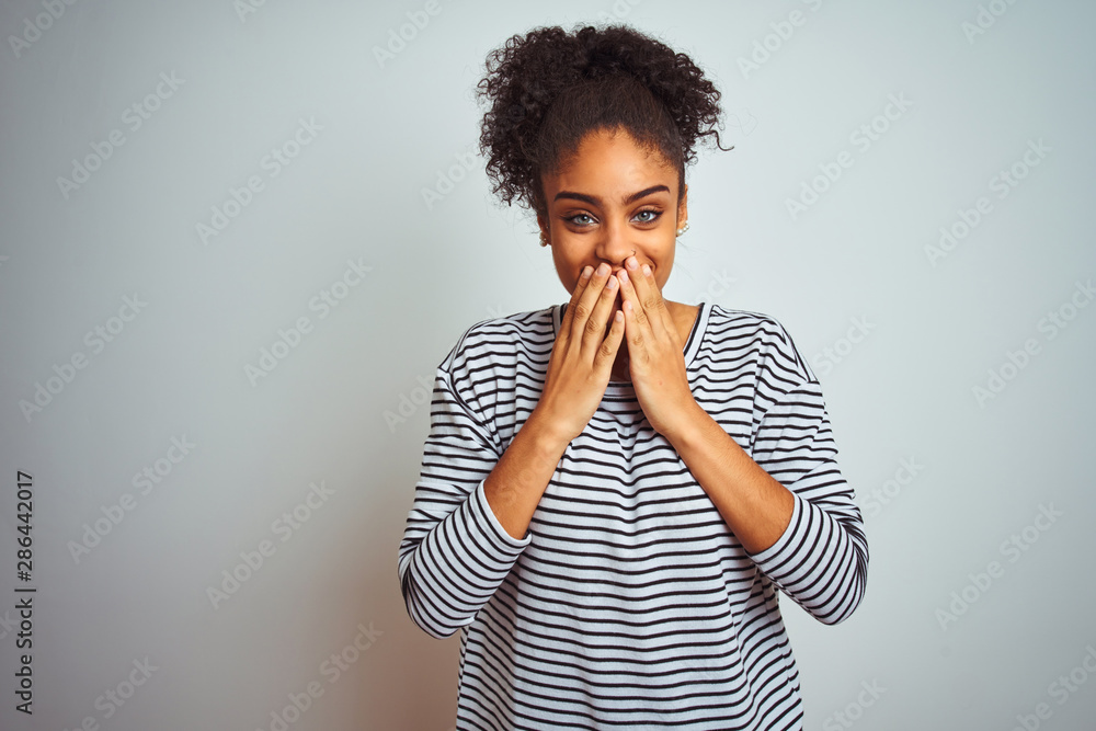 African american woman wearing navy striped t-shirt standing over isolated white background laughing and embarrassed giggle covering mouth with hands, gossip and scandal concept - obrazy, fototapety, plakaty 