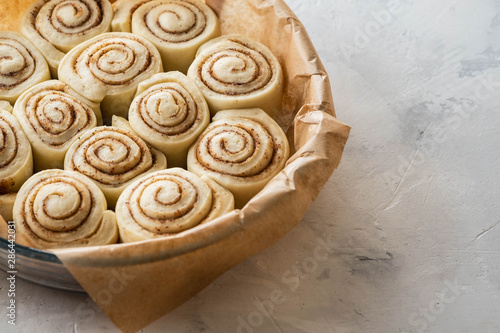 Raw cinnamon rolls in baking plate on kitchen table. Copy space.